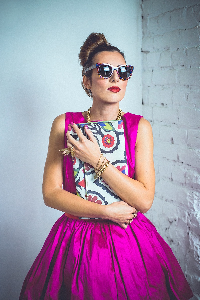 Ona u magenta haljini sa šarenim naočarima i folk-print torbicom