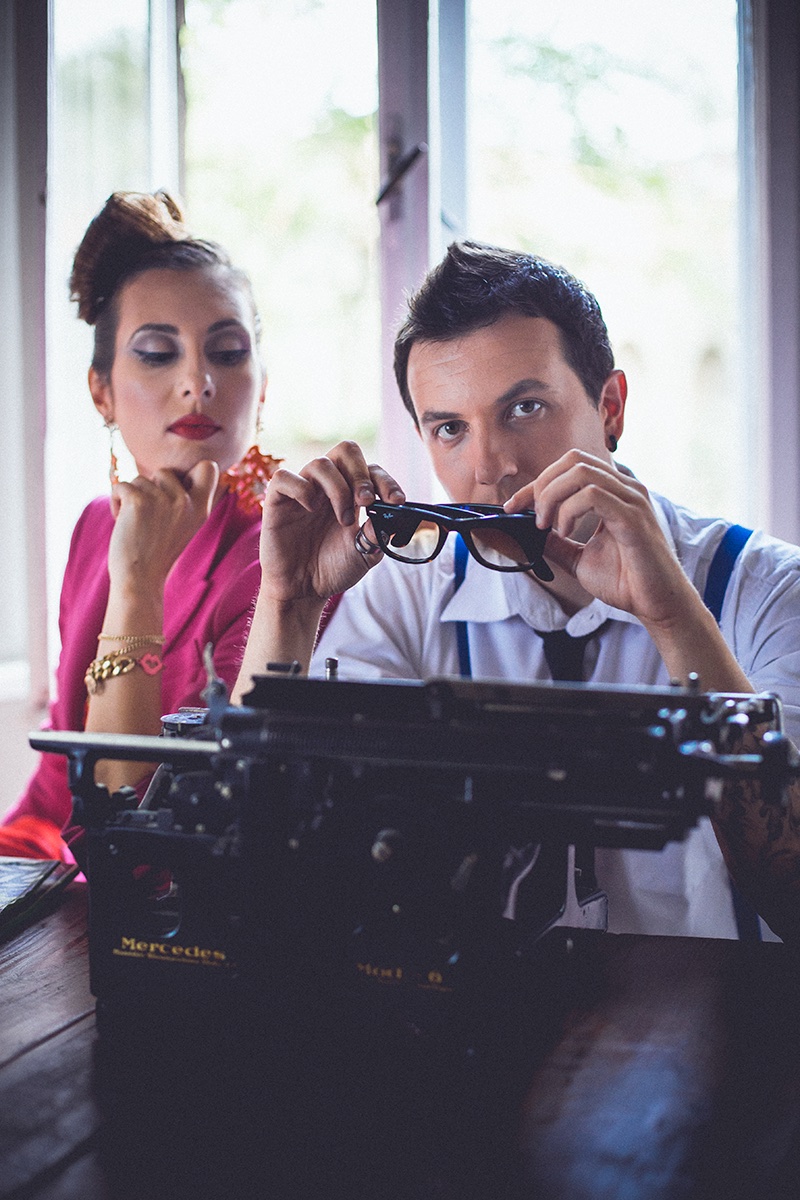 Par za vintage Mercedes pisaćom mašinom — on drži naočare, ona u magenta haljini
