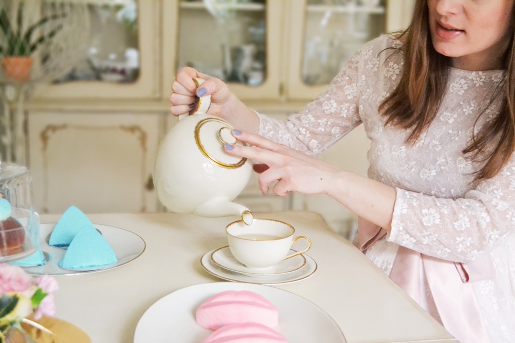 Sipanje čaja u porcelanski šoljicu — ružičasti kolači i pastelna dekoracija